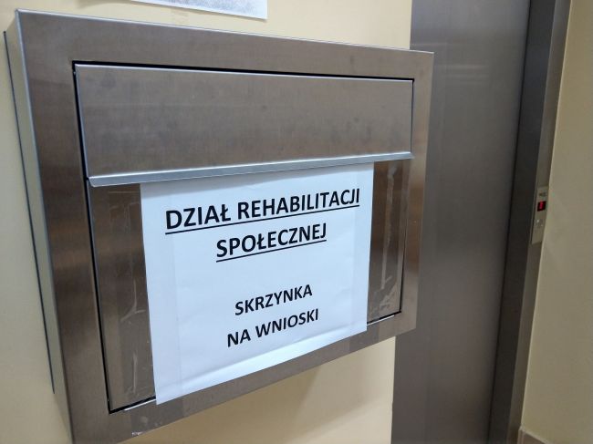 Powiększ zdjęcie: Zdjęcie przedstawia srebrną skrzynkę z przyklejoną kartką z napisem "Dział Rehabilitacji Społecznej - skrzynka na wnioski". Zawieszonej  przy windzie. 