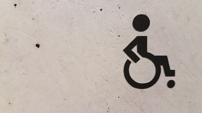 Powiększ zdjęcie: Zdjęcie przedstawia fragment sciany, a na niej czarny znak osoby niepełnosprawnej na wózku. Fot. Licencja CCO (domena publiczna, Unsplash)
