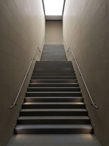 Powiększ zdjęcie: Zdjęcie przedstawia strome schody, po bokach dlugie srebrne barierki, przymocowane do ścian.  Fot. Licencja CCO (domena publiczna, Unsplash)