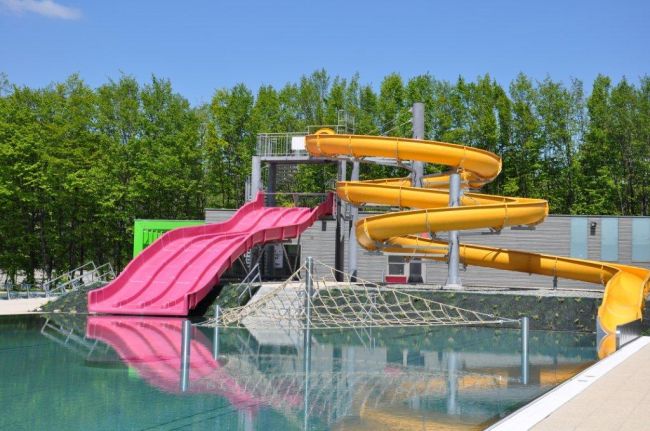 Powiększ zdjęcie: Zdjęcie przedstawia basen z dwie zjeżdżalniami: różową po lewej i żółtą po prawe stronie.   Źródło: http://www.bbosir.bielsko.pl/obiekt/plywalnia-start